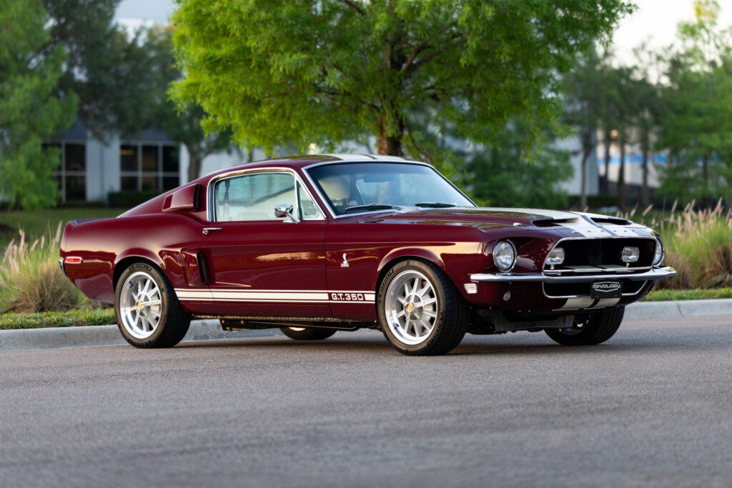 Maroon 1968 Shelby GT350 Fastback with white racing stripes parked on a tree-lined road.